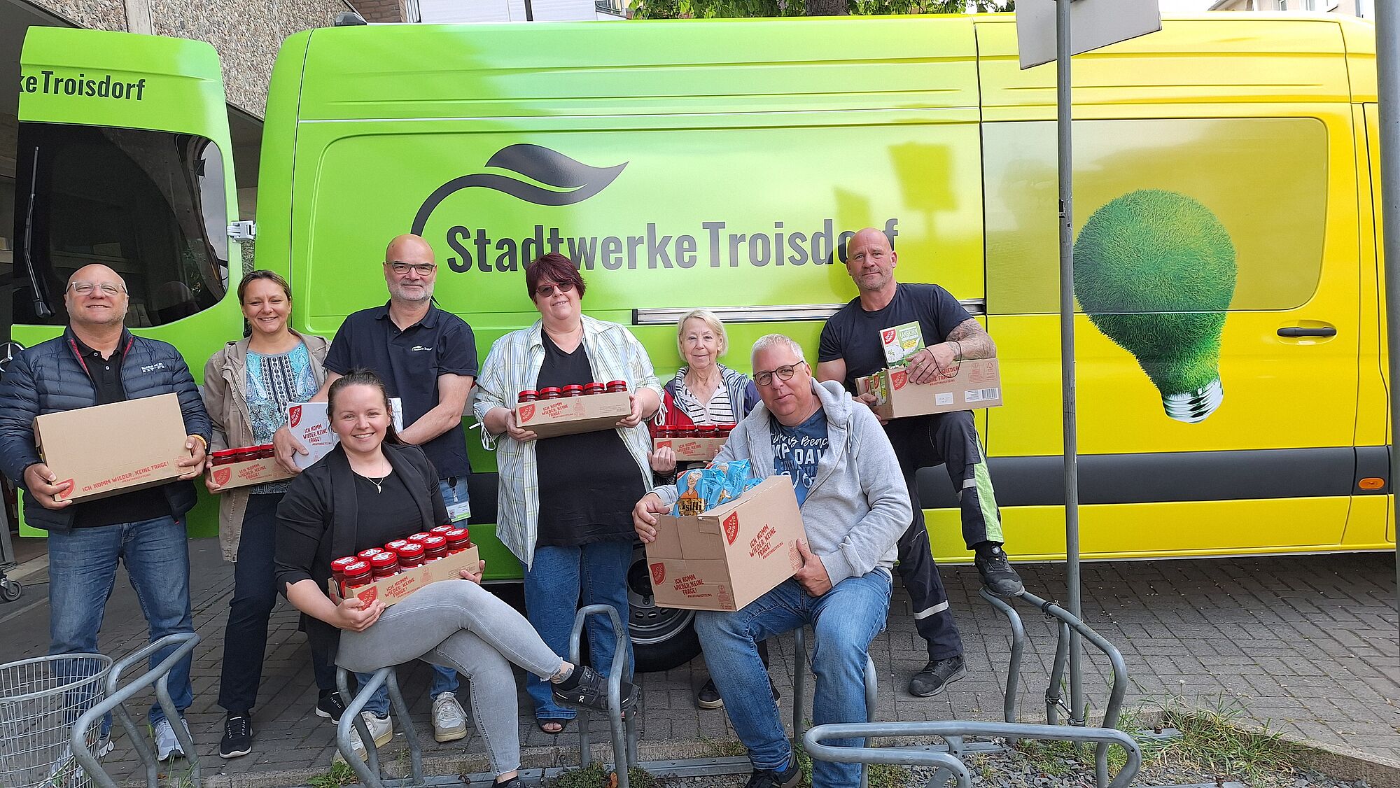 Tafel-Mitarbeiterin gemeinsam mit Stadtwerke-Betriebsrat vor dem Stadtwerke-Auto mit den Lebensmittelspenden im Arm