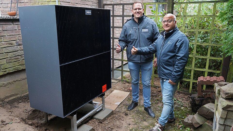 Zwei Mitarbeiter stehen an einer neuen Wärmepumpe und zeigen den Daumen nach oben