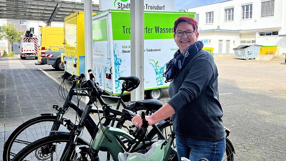 Mitarbeiterin steht auf dem Betriebshof an ihrem Fahrrad und schaut in die Kamera