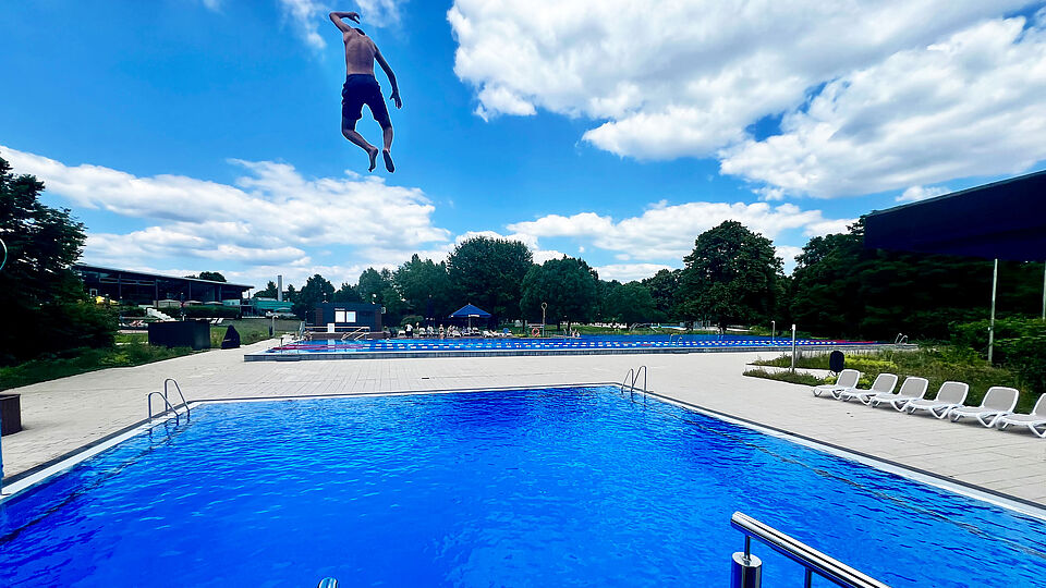 Mann springt vor der AGGUA-Freibad-Kulisse ins Becken