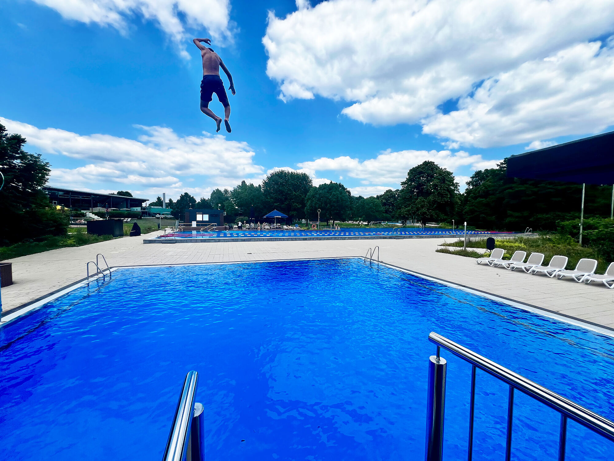 Sprung vom Turm ins Becken im AGGUA Mann springt vor der AGGUA-Freibad-Kulisse ins Becken