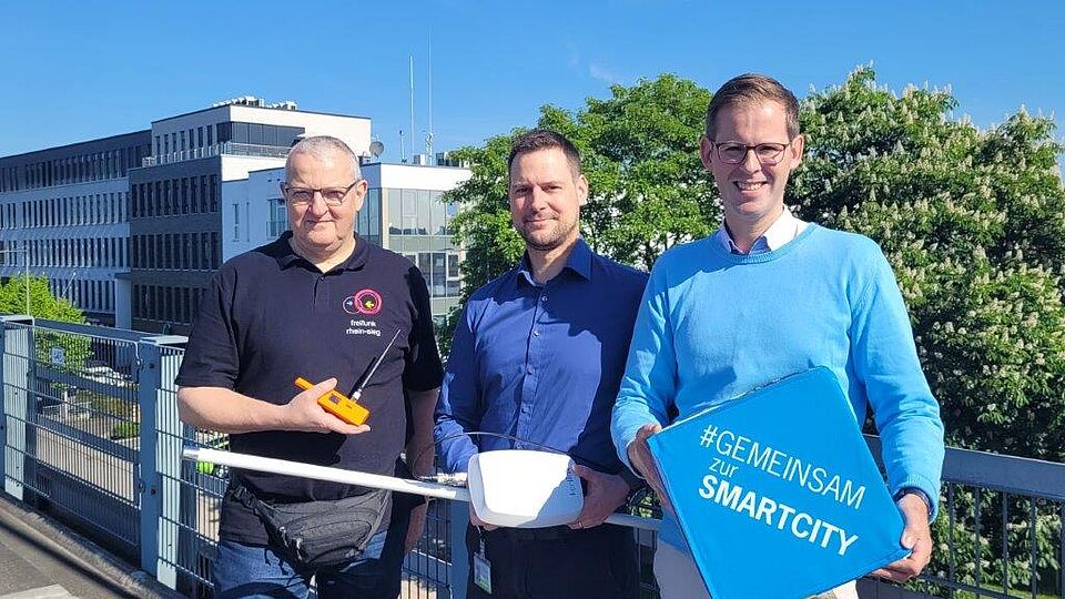 Gruppenbild: Andreas Gross, Christian Krueger und Fabian Wagner stehen vor Antennen auf Gebäudedächern.