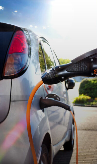 Silbernes Auto wird mit orangenem Kabel, an Ladesäule aufgeladen 