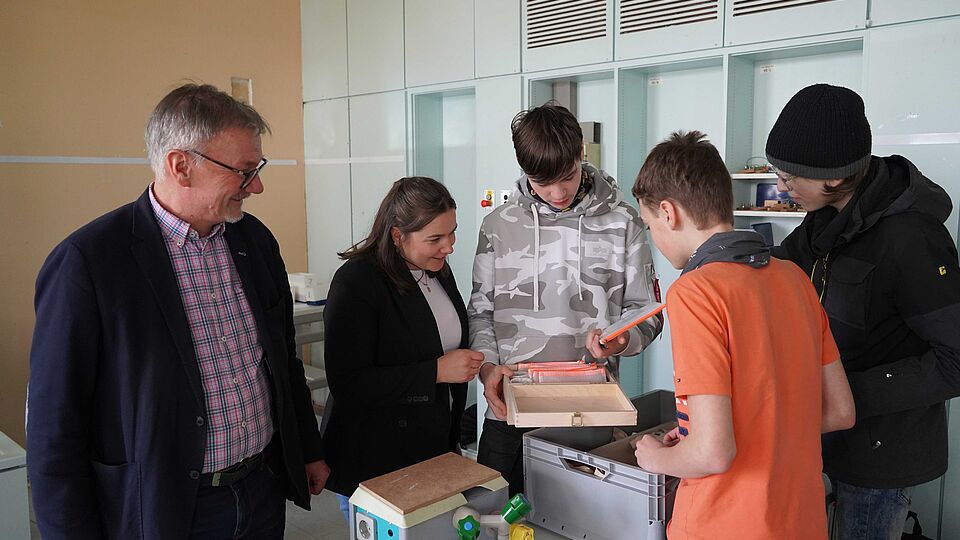 Schulleiter, Stadtwerke-Vertreterin und Schüler nehmen im Klassenraum die neu angeschafften Klimakoffer in Augenschein. 
