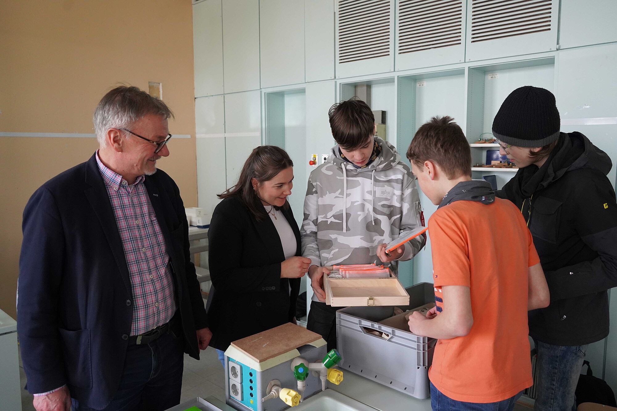 Schulleiter, Stadtwerke-Vertreterin und Schüler nehmen im Klassenraum die neu angeschafften Klimakoffer in Augenschein.