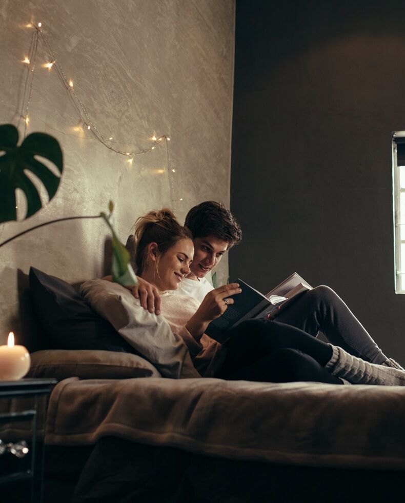 Paar liegt gemütlich beisammen und liest ein Buch 