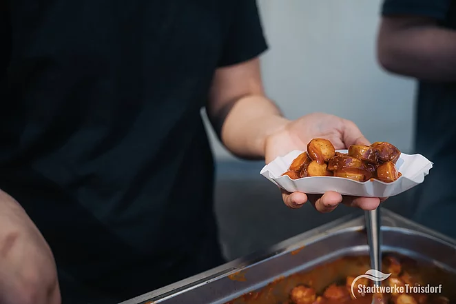 Schale mit Currywurst in einer Hand