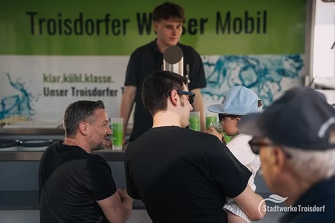Männer mit Kind bestellen Wasser am Wasserwagen