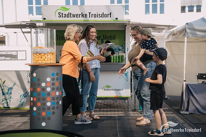 Stadtwerkemitarbeiterin und Geschäftsführerin übergeben Siegerurkunde an Frau mit zwei Kindern