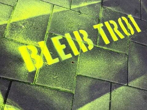 gelbe Graffiti-Schrift auf dem Boden Grüner Bleib Troi Schriftzug auf Straße