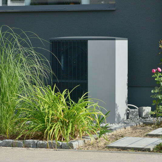 Wärmepumpe vor dem Haus Wärmepumpe vor einem Haus umgeben von einem Zaun und eine Pflanze