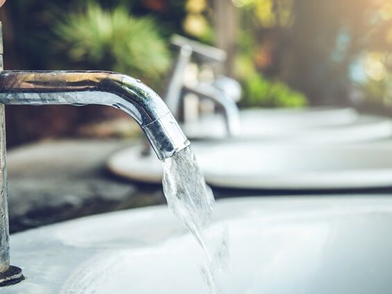 Wasserhahn mit fließendem Wasser im Vordergrund, während im Hintergrund mehrere Wasserhähne und eine grüne Landschaft zu sehen sind