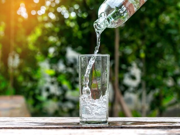  Ein Glas wird mit Wasser gefüllt, umgeben von einer grünen Landschaft