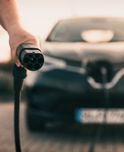 Mann hält Stecker in der Hand um E-Auto zu laden 
