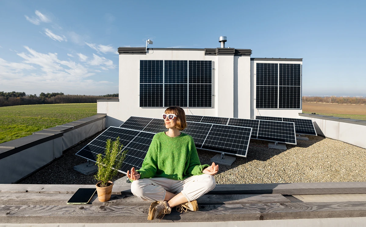 Eine Frau mit Sonnenbrille sitzt im Schneidersitz vor einigen Solarmodulen und schaut in die Sonne