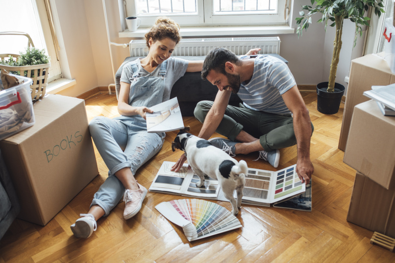 Familie mit Hund zieht in neues Zuhause Ein junges Paar mit einem Hund sitzt auf dem Boden und schaut sich ein Katalog an