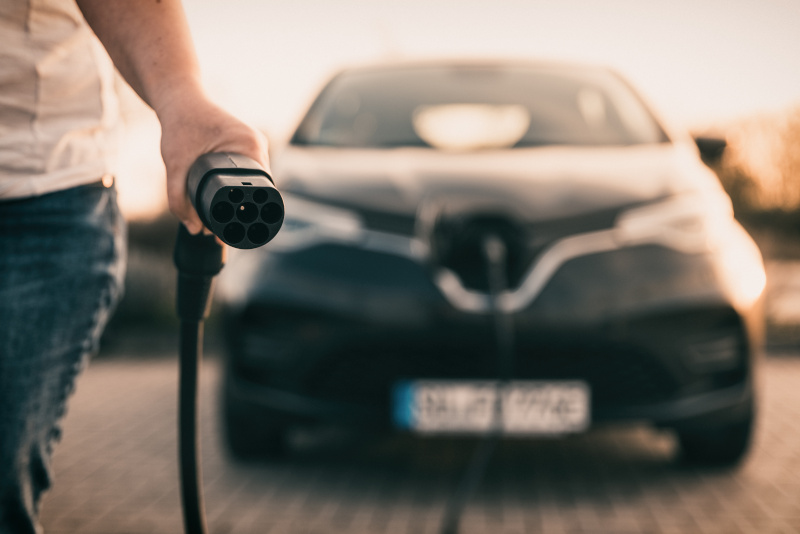 E-Auto wird geladen Mann hält Stecker in der Hand um E-Auto zu laden