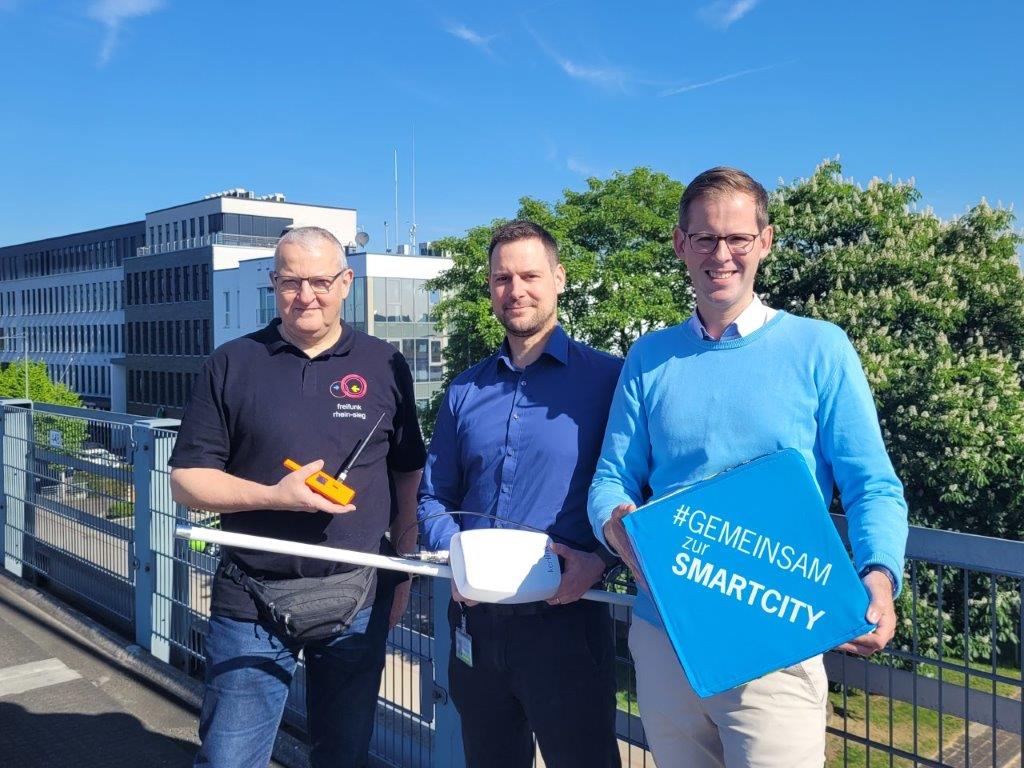 Gruppenbild: Andreas Gross, Christian Krueger und Fabian Wagner stehen vor Antennen auf Gebäudedächern.